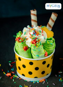 Green ice cream rolls with vanilla and chocolate wafer rolls, sprinkles, and frosting in a yellow and black poka dot container from freepik.com