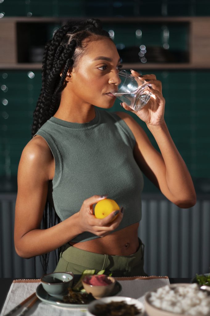 LADY DRINKING WATER FROM A GLASS CUP HOLDING A LEMON FROM FREEPIK.COM